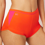 Ikonō’s orange high-waist shorty bikini, perfect for water sports, Pilates, or yoga. Made with recycled materials and UPF50+ protection, combining comfort, style, and support for every woman.