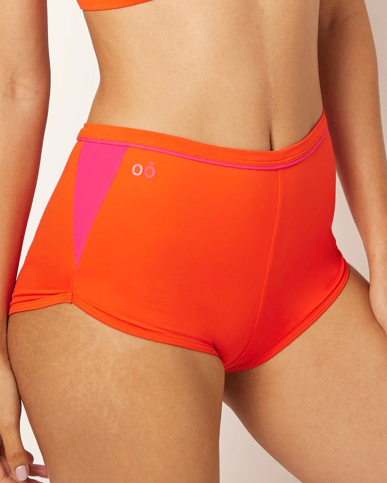 Ikonō’s orange high-waist shorty bikini, perfect for water sports, Pilates, or yoga. Made with recycled materials and UPF50+ protection, combining comfort, style, and support for every woman.