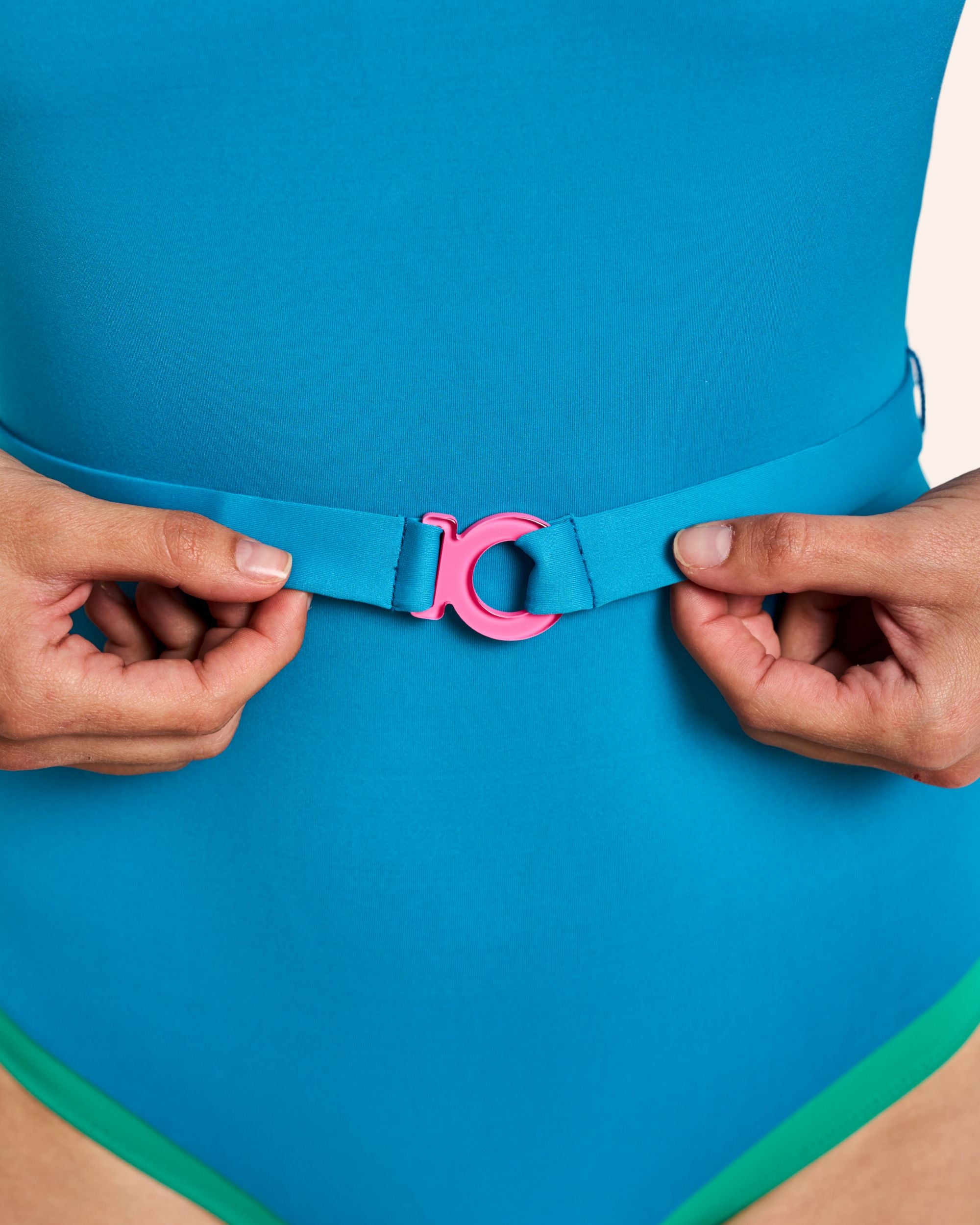 Maillot ikonō Allure Bleu Vert Emeraude, modèle de face en studio, zoom sur ceinture amovible et logo rose signature